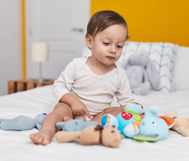 Αξιολάτρευτο ισπανόφωνο αγόρι που κάθεται στο κρεβάτι με κούκλες στην κρεβατοκάμαρα - Φωτογραφία, εικόνα