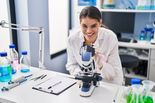 Joven hermosa mujer hispana científica usando microscopio en laboratorio - Foto, imagen