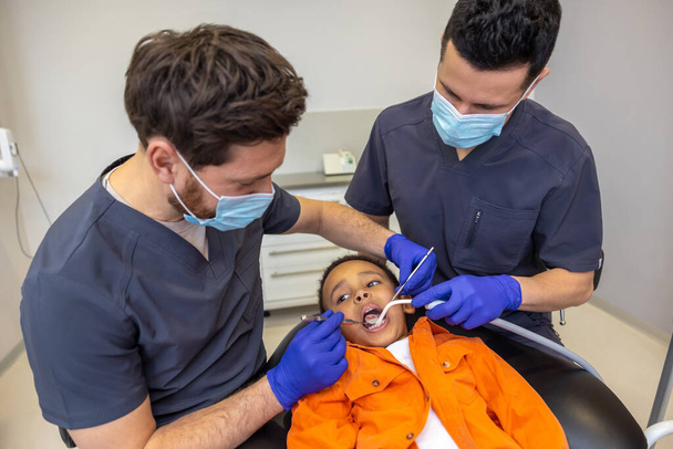 In dentistry. Dentist and his assistant working with a dark-skinned boy - Fotó, kép