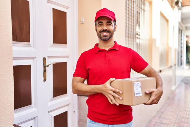 Young hispanic man courier holding package at street - Photo, Image