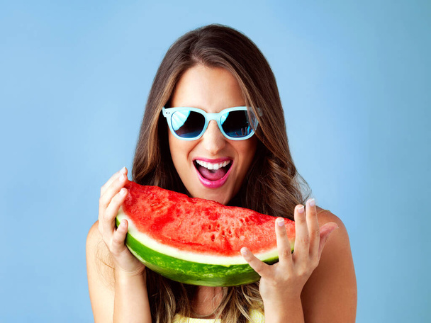 Du bringst die Sonne, ich die Wassermelone. Studioaufnahme einer attraktiven jungen Frau, die vor blauem Hintergrund posiert - Foto, Bild