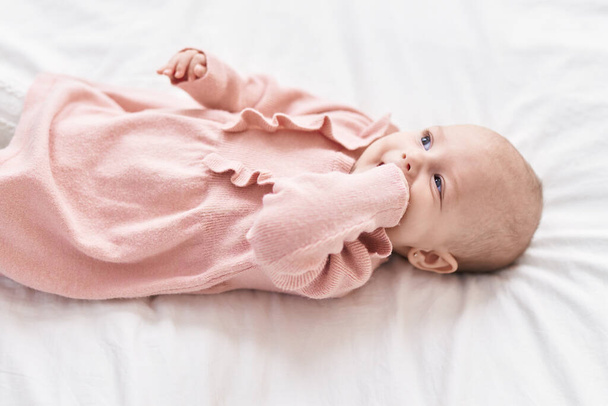Adorable bébé caucasien couché sur le lit morsure main à la chambre - Photo, image