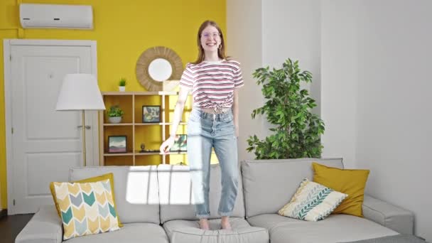 Jeune femme blonde souriante danse confiante sur le canapé à la maison - Séquence, vidéo