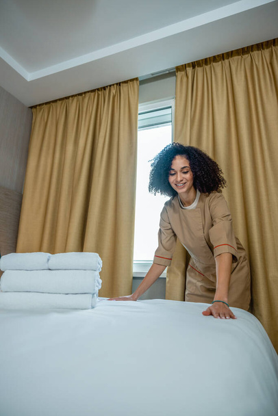 Making bed. Curly-haired young woman making bed on a hotel room - Foto, immagini