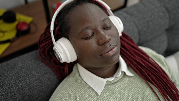 Αφρικανική γυναίκα με πλεγμένα μαλλιά ακούγοντας μουσική ξαπλωμένη στον καναπέ στο σπίτι - Φωτογραφία, εικόνα