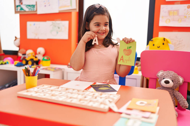 Entzückendes hispanisches Mädchen spielt mit Vokabelpuzzle-Spiel, das im Kindergarten auf dem Tisch sitzt - Foto, Bild