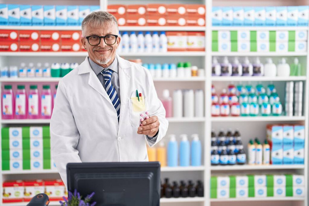 Keski-ikä harmaa tukka mies farmaseutti holding pillereitä tabletti tietokoneella laboratoriossa - Valokuva, kuva