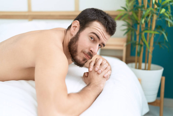 Nuori latino mies hymyilee luottavainen makaa sängyssä makuuhuoneessa - Valokuva, kuva
