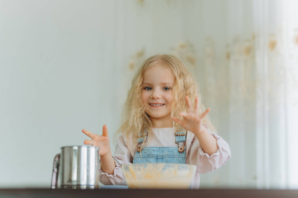 ベーキング用の食材を持った小さな女の子. 子供は食べ物,クッキーを用意しています. 子供は楽しく,料理することを学び,キッチンで遊ぶ. - 写真・画像