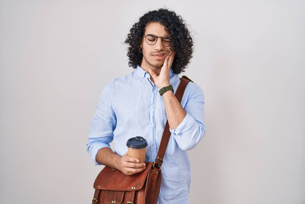 Hispanic man with curly hair drinking a cup of take away coffee touching mouth with hand with painful expression because of toothache or dental illness on teeth. dentist concept.  - Foto, afbeelding