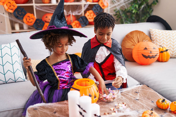 Imádnivaló afro-amerikai fiú és lány halloween jelmez gazdaság cukorka tál otthon - Fotó, kép