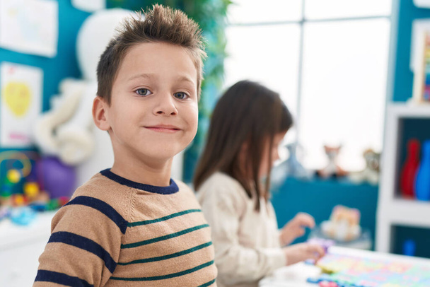 Rozkošný chlapec a dívka usměvavé sebevědomí sedí na stole ve školce - Fotografie, Obrázek