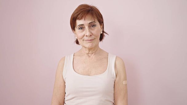 Ώριμη ισπανόφωνη γυναίκα με τσιρότο στο χέρι πάνω από απομονωμένο ροζ φόντο - Φωτογραφία, εικόνα