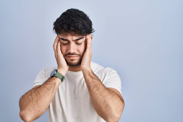 Homme hispanique avec la barbe debout sur fond blanc avec la main sur la tête, maux de tête parce que le stress. migraine souffrant.  - Photo, image
