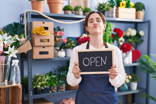 Brunette woman working at florist holding open sign looking at the camera blowing a kiss being lovely and sexy. love expression.  - Photo, Image