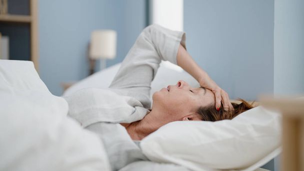 Latynoska kobieta w średnim wieku martwi się leżąc na łóżku w sypialni - Zdjęcie, obraz