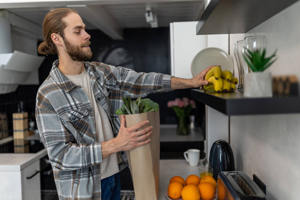 Mann packt nach Ladenbesuch Gemüse und Obst in Küche aus und kauft frische Produkte. - Foto, Bild