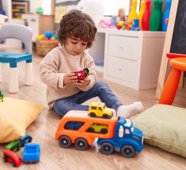 Uroczy latynoski chłopiec bawiący się zabawką samochodową siedzący na podłodze w przedszkolu - Zdjęcie, obraz