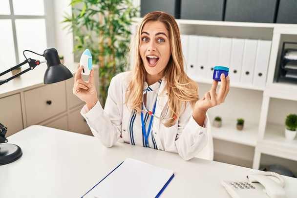 Young blonde doctor woman holding medicine products to breath better celebrating crazy and amazed for success with open eyes screaming excited.  - Фото, изображение