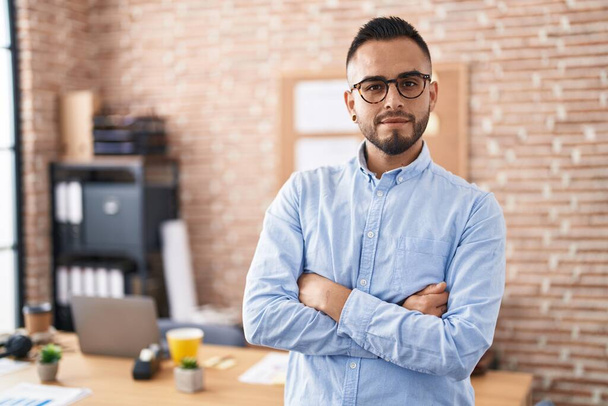 Young hispanic man business worker standing with arms crossed gesture at office - Photo, Image