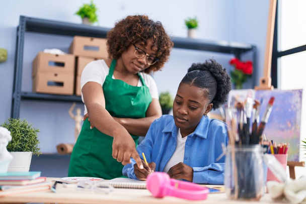 African american women teacher and student artist drawing on notebook at art studio - Photo, Image