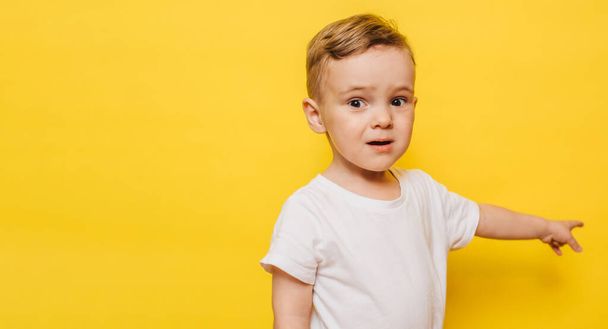 little boy on a yellow background points to the background. Copy space. - Foto, imagen
