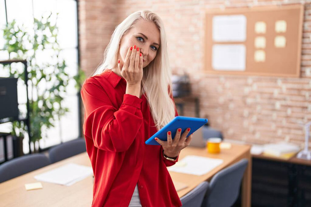 Běloška pracující v kanceláři s tabletou se smíchem a rozpačitým hihňáním zakrývajícím ústa rukama, drby a skandálním pojetím  - Fotografie, Obrázek