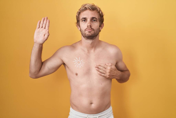 Kaukasischer Mann steht hemdlos in Sonnencreme und schwört mit der Hand auf Brust und Handfläche und leistet einen Treueschwur  - Foto, Bild