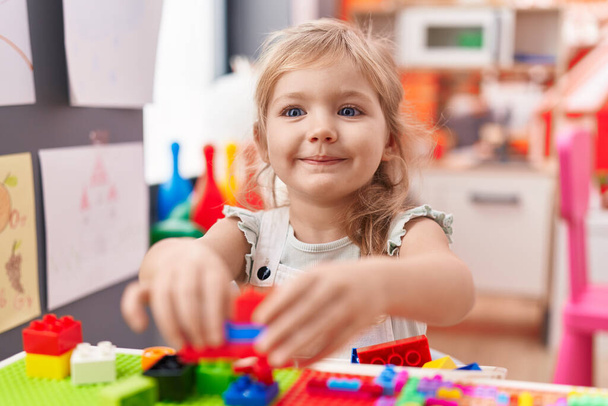 Adorable blonde girl playing with construction blocks sitting on table at kindergarten - Foto, imagen