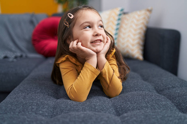 Liebenswertes hispanisches Mädchen lächelnd auf dem Sofa zu Hause - Foto, Bild