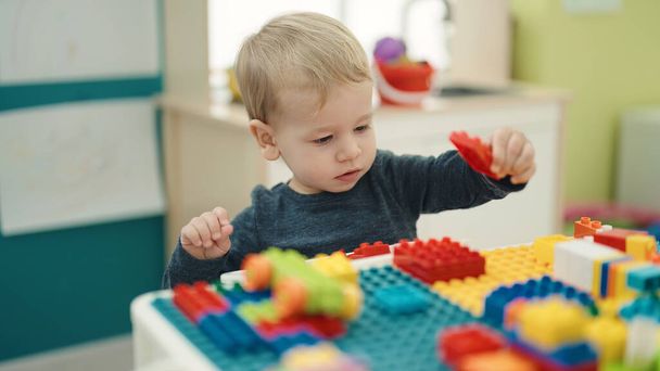 Liebenswertes blondes Kleinkind spielt im Kindergarten mit Bauklötzen am Tisch - Foto, Bild