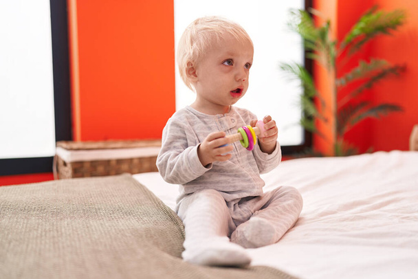Αξιολάτρευτο ξανθό νήπιο παίζει με παιχνίδια που κάθονται στο κρεβάτι στο υπνοδωμάτιο - Φωτογραφία, εικόνα