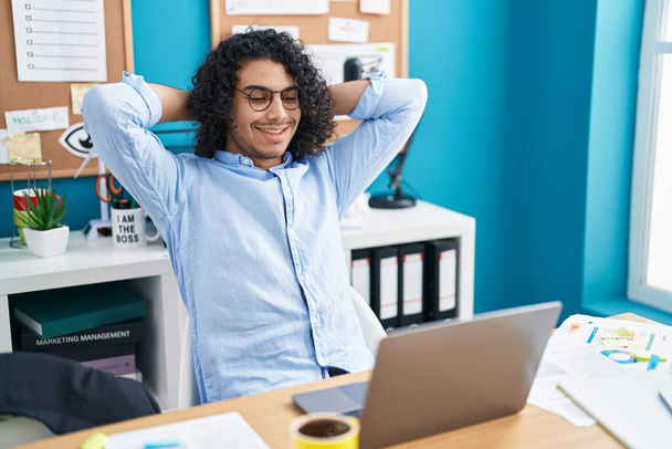 Young latin man business worker relaxed with hands on head at office - Fotoğraf, Görsel