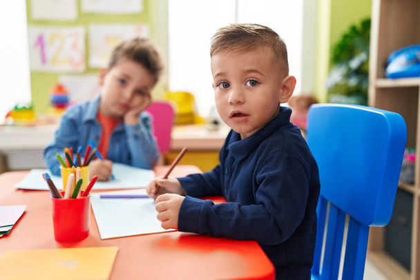 Чарівні хлопчики дошкільнята сидять на столі малюючи на папері в дитячому садку
 - Фото, зображення