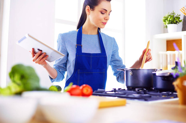 Young woman using a tablet computer to cook in her kitchen. - Foto, immagini