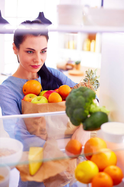 Smiling woman taking a fresh fruit out of the fridge, healthy food concept. - Foto, Imagem