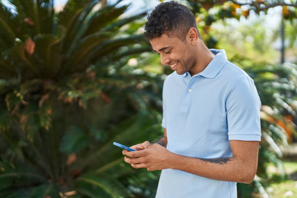 Afro-Amerikalı adam parkta akıllı telefon kullanarak kendine güveniyor. - Fotoğraf, Görsel