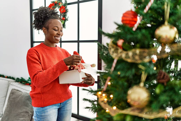 Αφροαμερικανή γυναίκα χαμογελά αυτοπεποίθηση διακόσμηση χριστουγεννιάτικο δέντρο στο σπίτι - Φωτογραφία, εικόνα