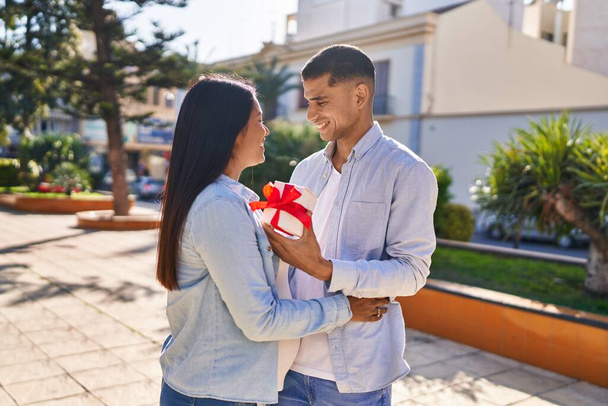 Young latin couple expecting baby surprise with gift at park - Zdjęcie, obraz