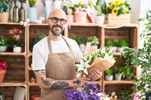 Young bald man florist holding bouquet of flowers at florist - Foto, imagen