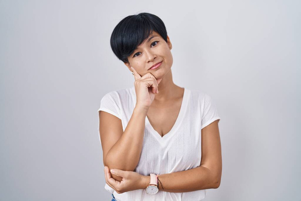 Young asian woman with short hair standing over isolated background with hand on chin thinking about question, pensive expression. smiling with thoughtful face. doubt concept.  - Foto, immagini