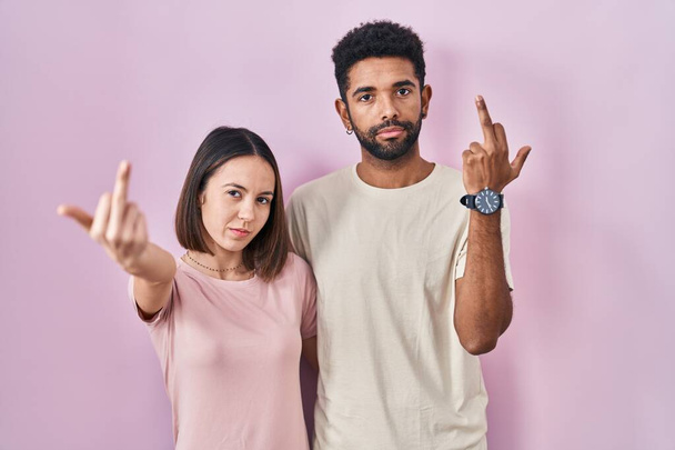 Молода пара іспаномовних пара разом над рожевим тлом, що показує середній палець, неввічливий і грубий хуй вираз
  - Фото, зображення