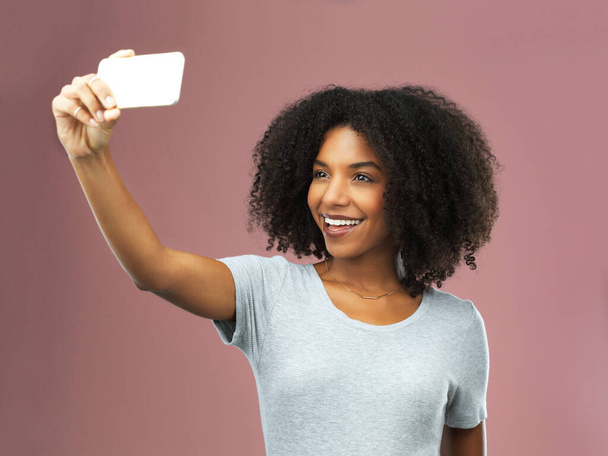 Wees trouw aan je selfie. Studio shot van een aantrekkelijke jonge vrouw het nemen van een selfie tegen een roze achtergrond - Foto, afbeelding