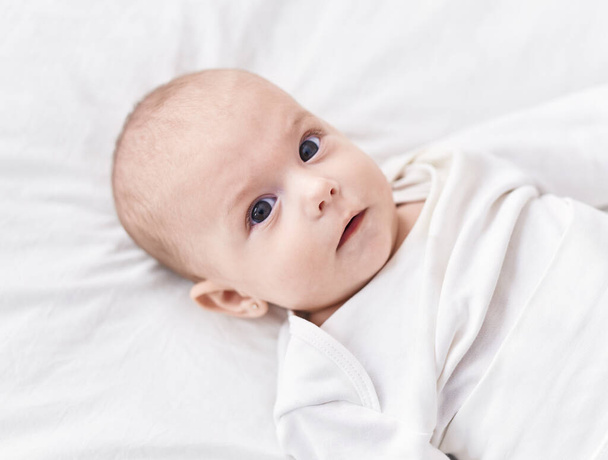 Adorable bébé caucasien couché sur le lit avec une expression détendue dans la chambre - Photo, image