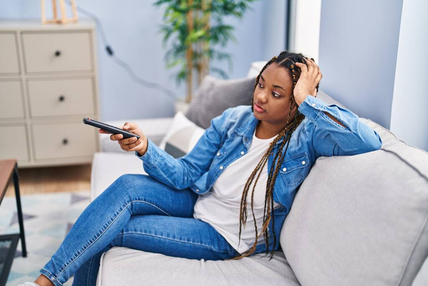 African american woman watching tv sitting on sofa with boring expression at home - Foto, immagini