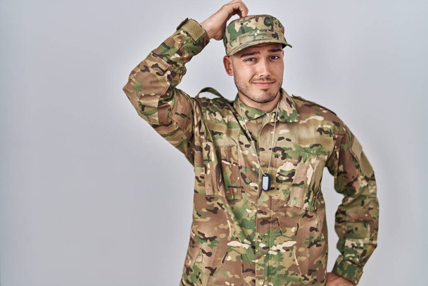 Un joven hispano vestido con uniforme camuflaje del ejército confunde y se pregunta acerca de la pregunta. incierto con la duda, pensando con la mano en la cabeza. concepto pensativo.  - Foto, imagen
