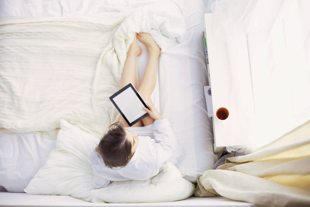 Retrato de mulher usando tablet e beber café enquanto se senta na cama pela manhã. - Foto, Imagem