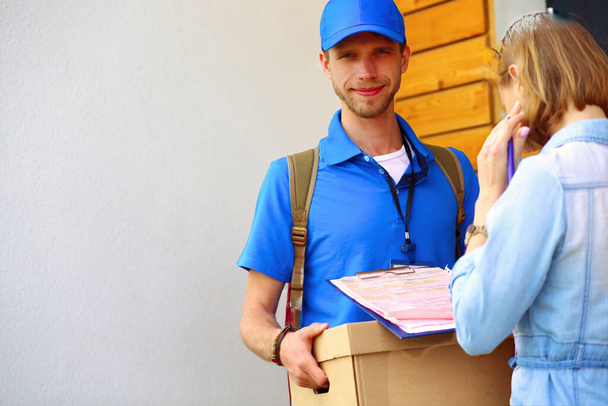 Smiling delivery man in blue uniform delivering parcel box to recipient - courier service concept. Smiling delivery man in blue uniform. - Fotoğraf, Görsel