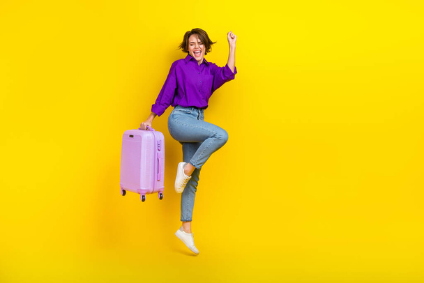 Full length photo of wearing purple shirt bob hair woman fist up hold baggage shopping before flight isolated on yellow color background. - Zdjęcie, obraz
