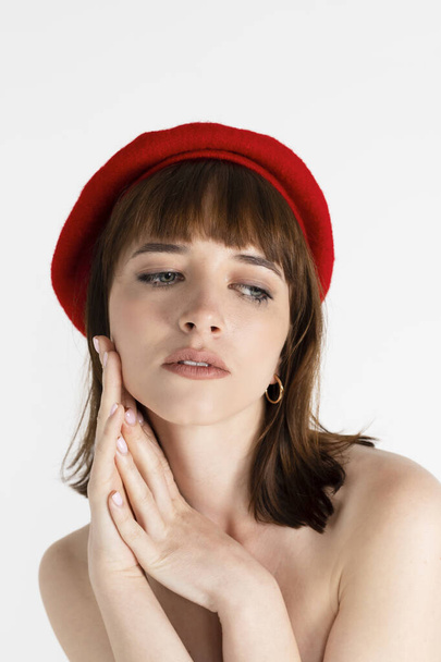 Young beautiful girl only in red tight and a beret, covering her bare chest. Sensual slim girl posing topless. Isolated on white background. Portrait, head shot. - Fotografie, Obrázek